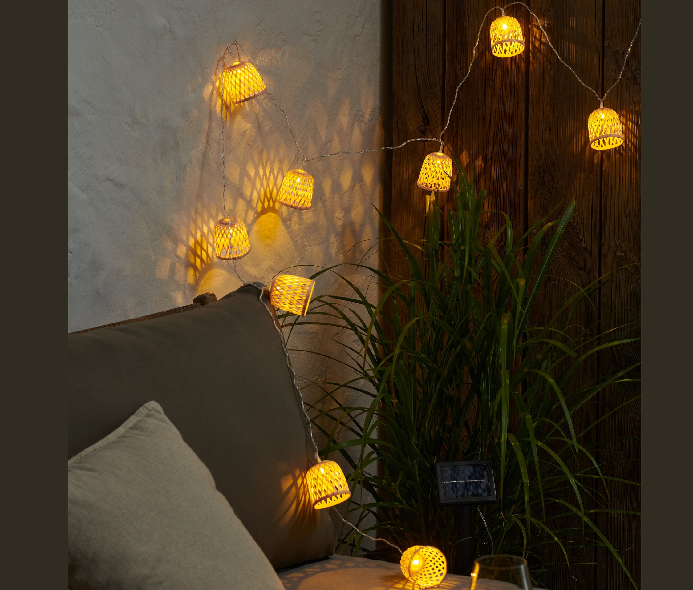 Une guirlande lumineuse solaire éclairée avec des abat-jour décoratifs suspendue au-dessus d'un canapé gris.