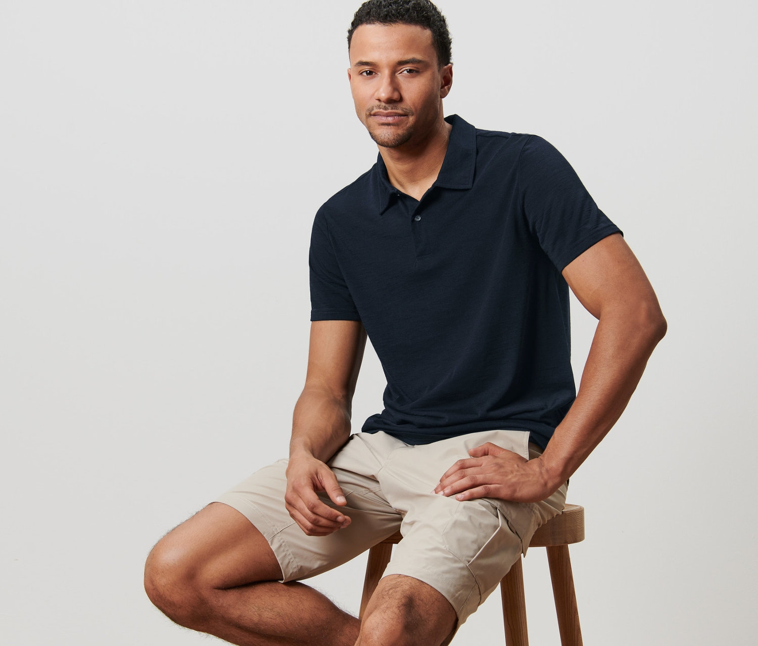 Un homme est assis sur un tabouret et porte un polo technique avec de la laine mérinos.