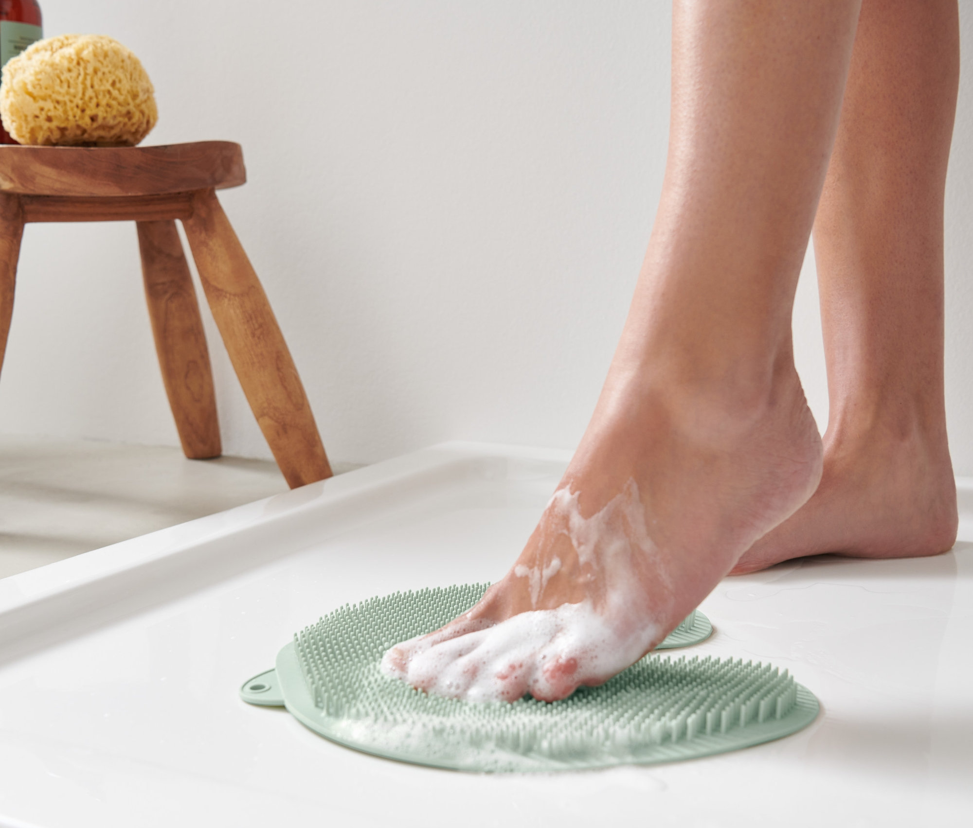 Un pied se savonne sur un tapis de nettoyage et de massage des pieds dans une douche blanche.