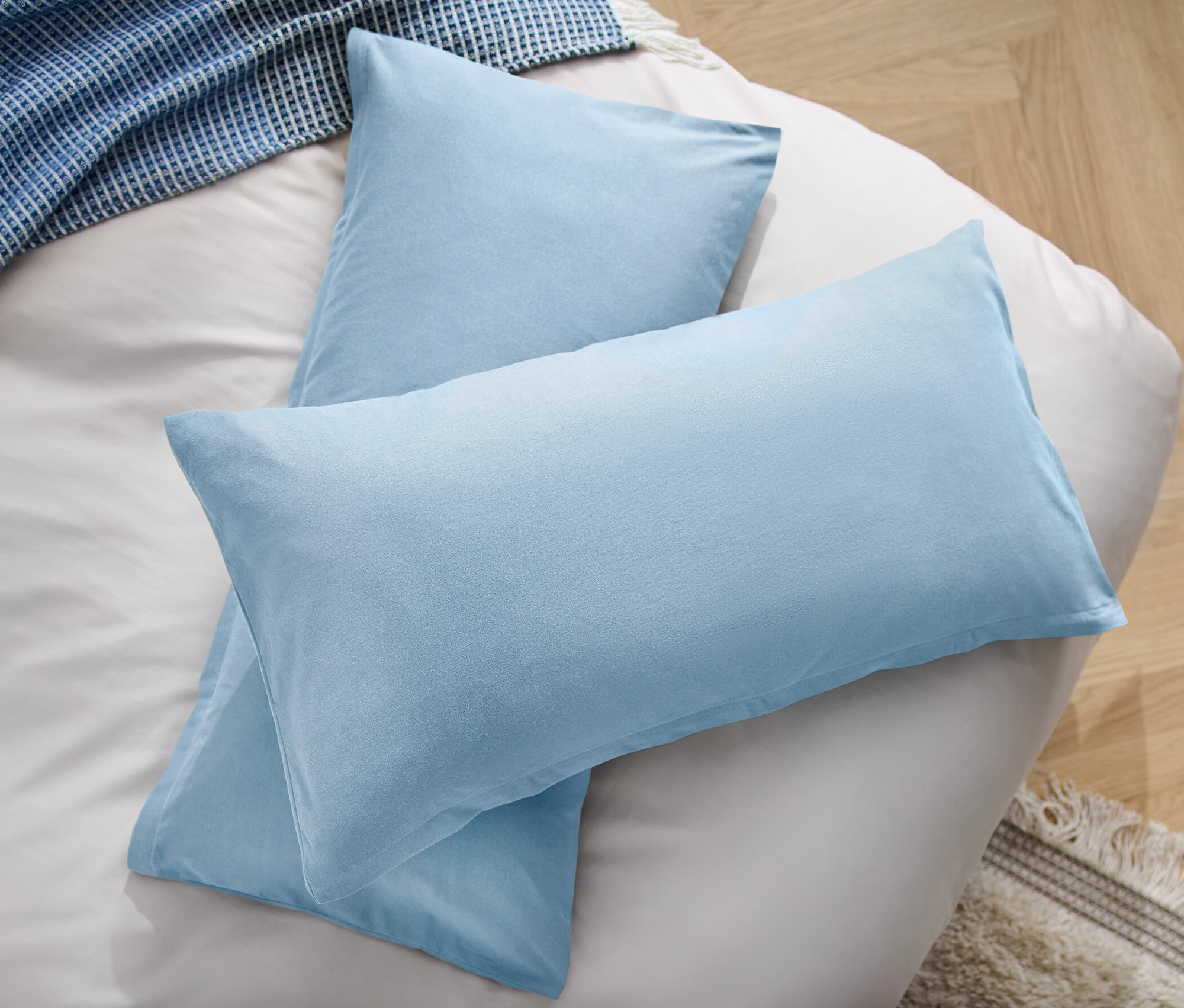 Deux taies d’oreiller en microfibre bleu clair sont posées sur un lit à côté d’une couverture bleue.