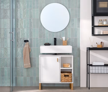 Salle de bain moderne avec carrelage vert menthe. À gauche, une cabine de douche et des toilettes. À droite, un meuble sous-vasque blanc avec lavabo et miroir rond. À côté, une armoire murale noire avec porte en verre et une console étroite noire avec étagères.
