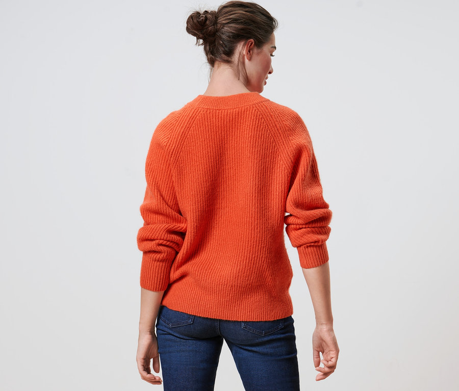 Vue arrière d'une femme portant un pull en maille orange et un jean.