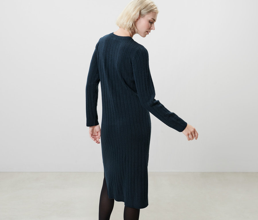 Blonde posant en robe en tricot côtelée bleu foncé.