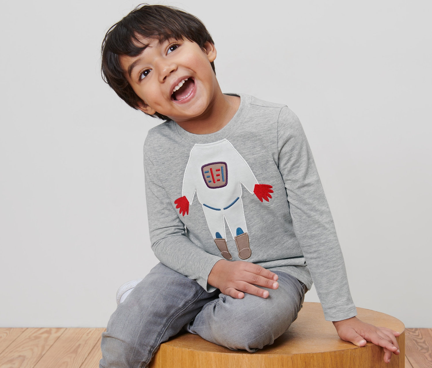 Un garçon est assis sur un tabouret en bois et porte un t-shirt gris à manches longues avec un motif d'espace.