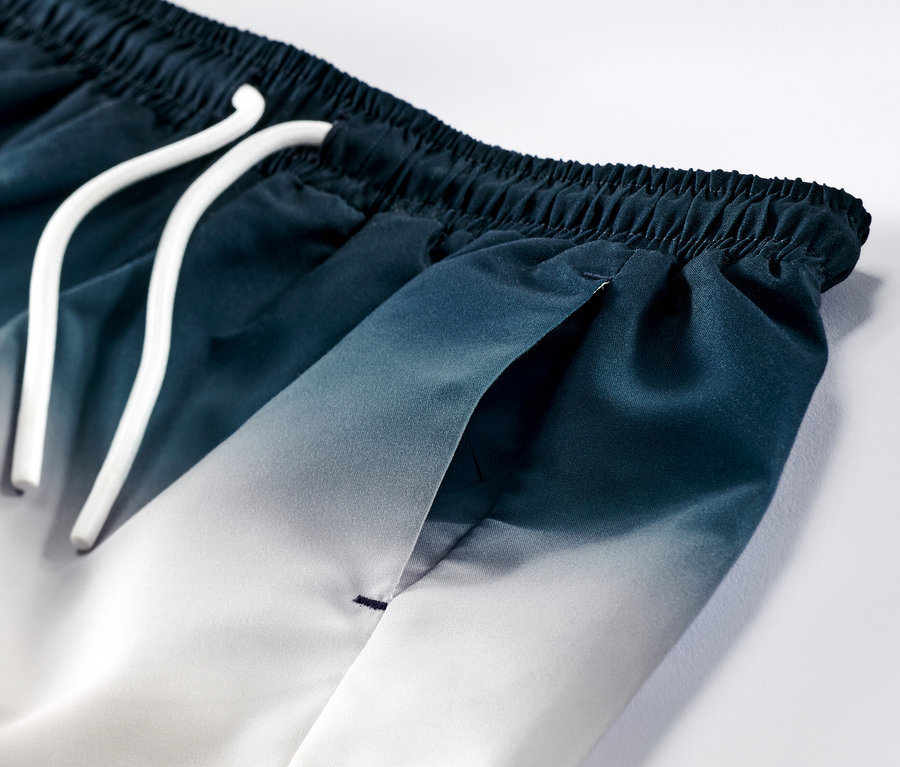 Gros plan sur un boardshort pour enfant avec un dégradé bleu et blanc et un cordon blanc.