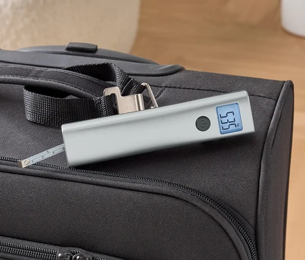 Une balance numérique pour valises est posée sur une valise noire.