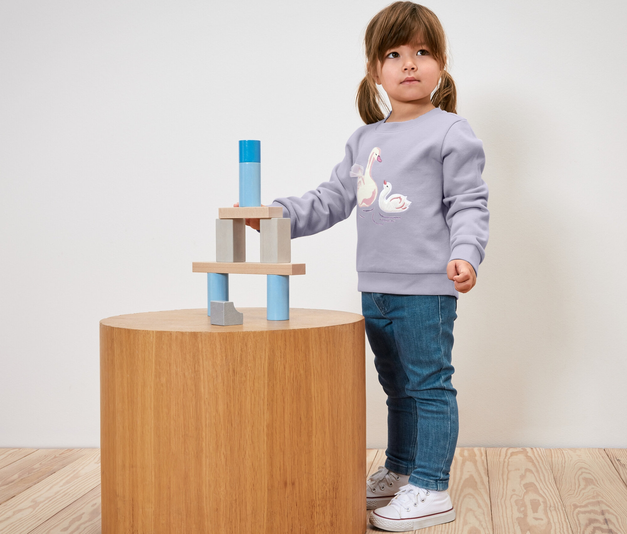 Une petite fille joue avec des blocs de bois sur une table ronde. Elle porte un Jean pour enfant ‒ Fit « Lotta ».