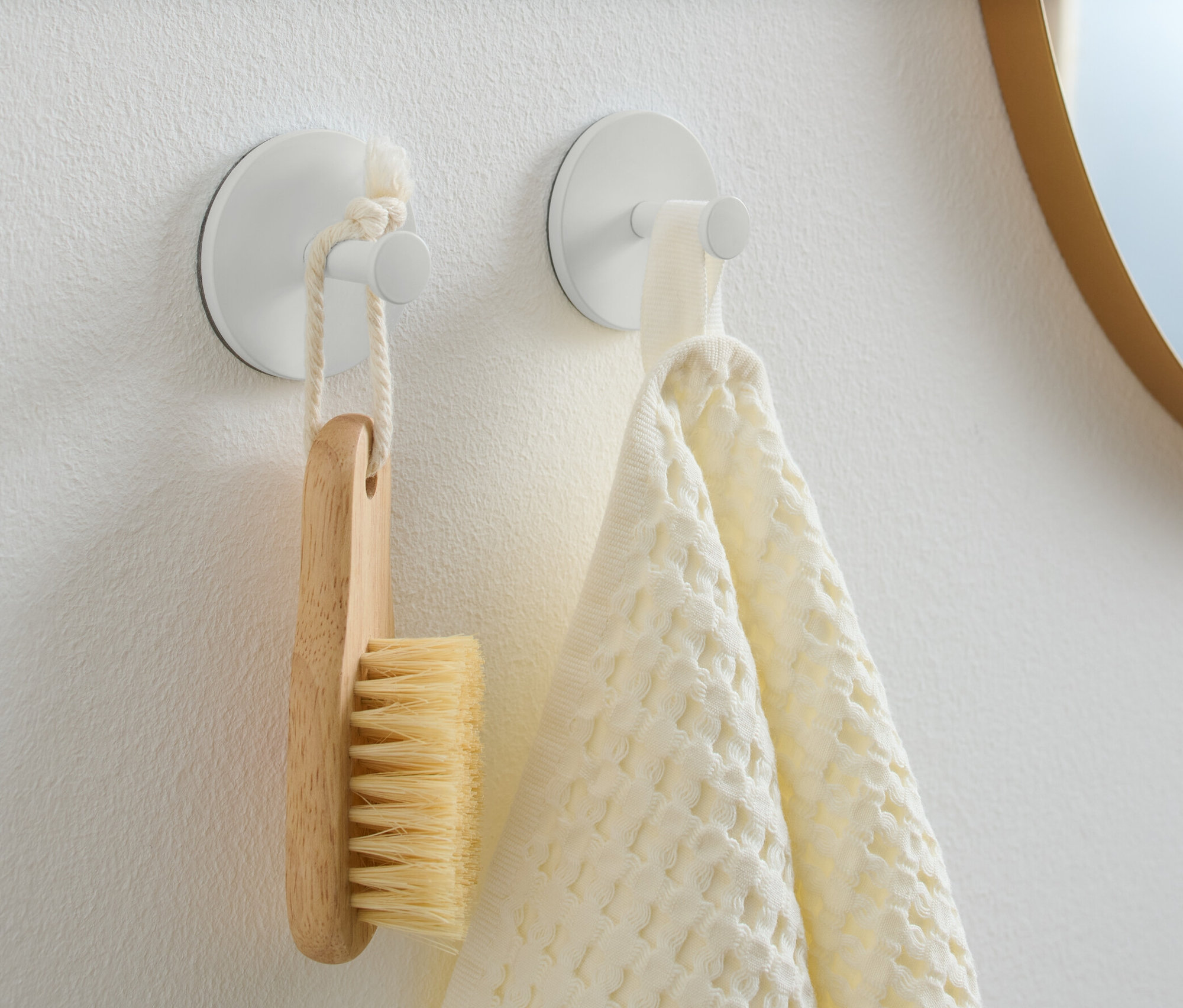 Deux crochets sont fixés sur un mur blanc. Une brosse en bois est suspendue à l’un d’eux et une serviette blanche à l’autre.