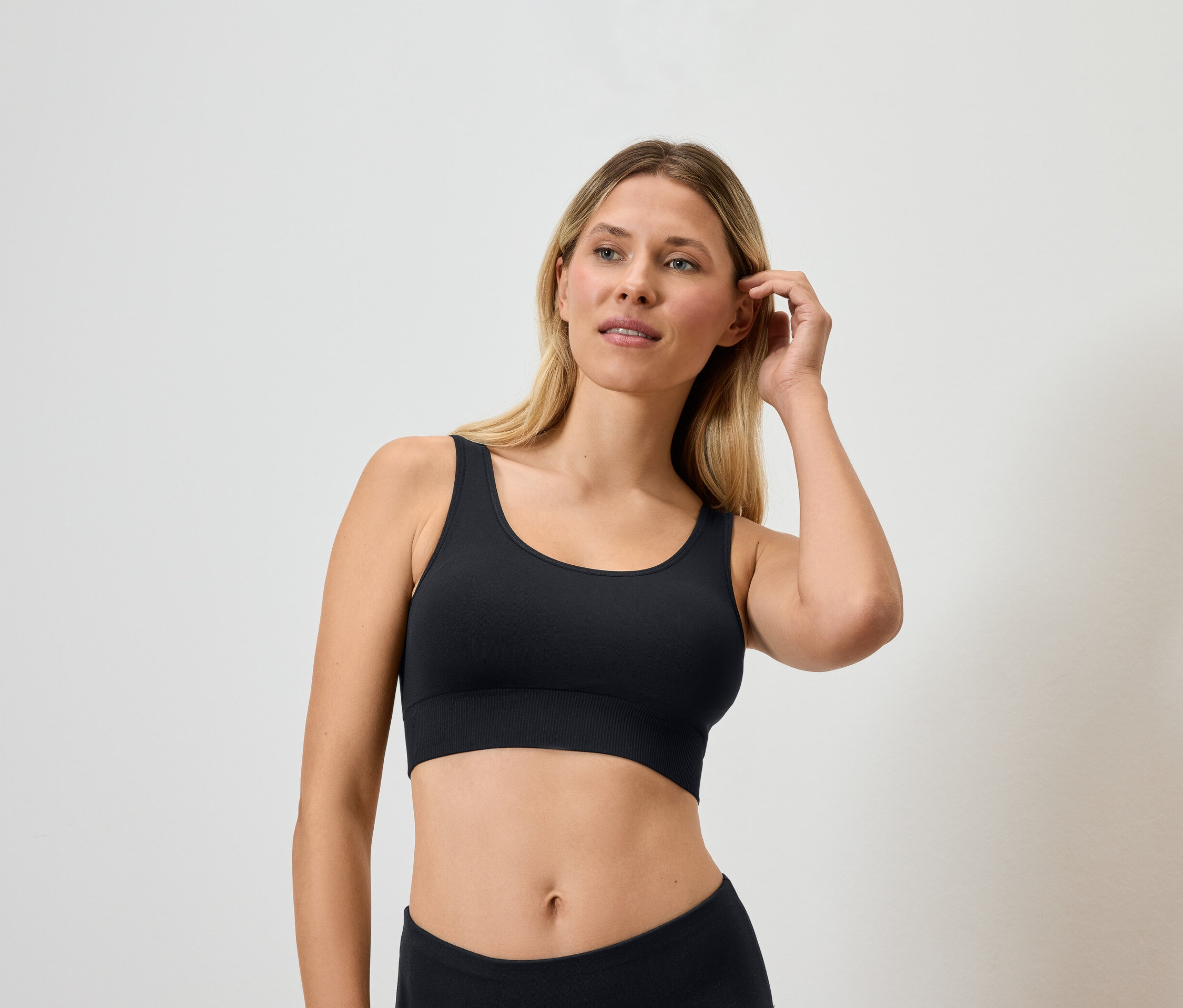 Blonde portant une brassière de sport noire et touchant ses cheveux.