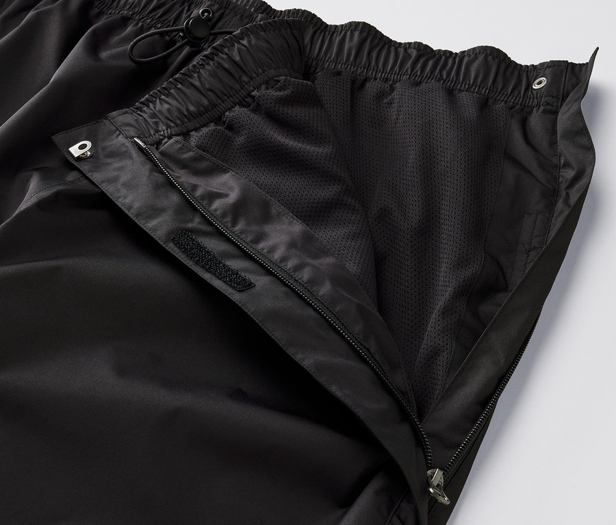 Gros plan sur un pantalon de pluie high-tech noir avec une fermeture éclair ouverte et une doublure en maille visible.