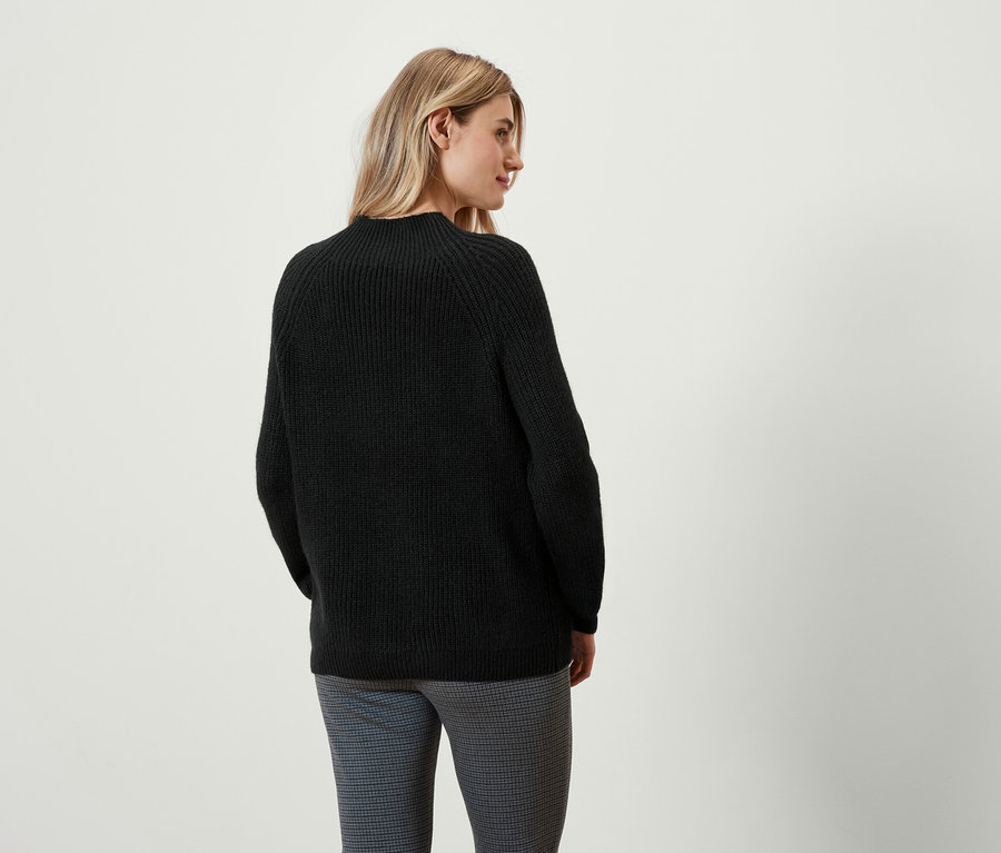 Une femme regarde par-dessus son épaule, portant un pull noir et un pantalon.