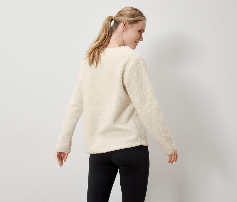 Une femme porte un pull crème et un legging noir.