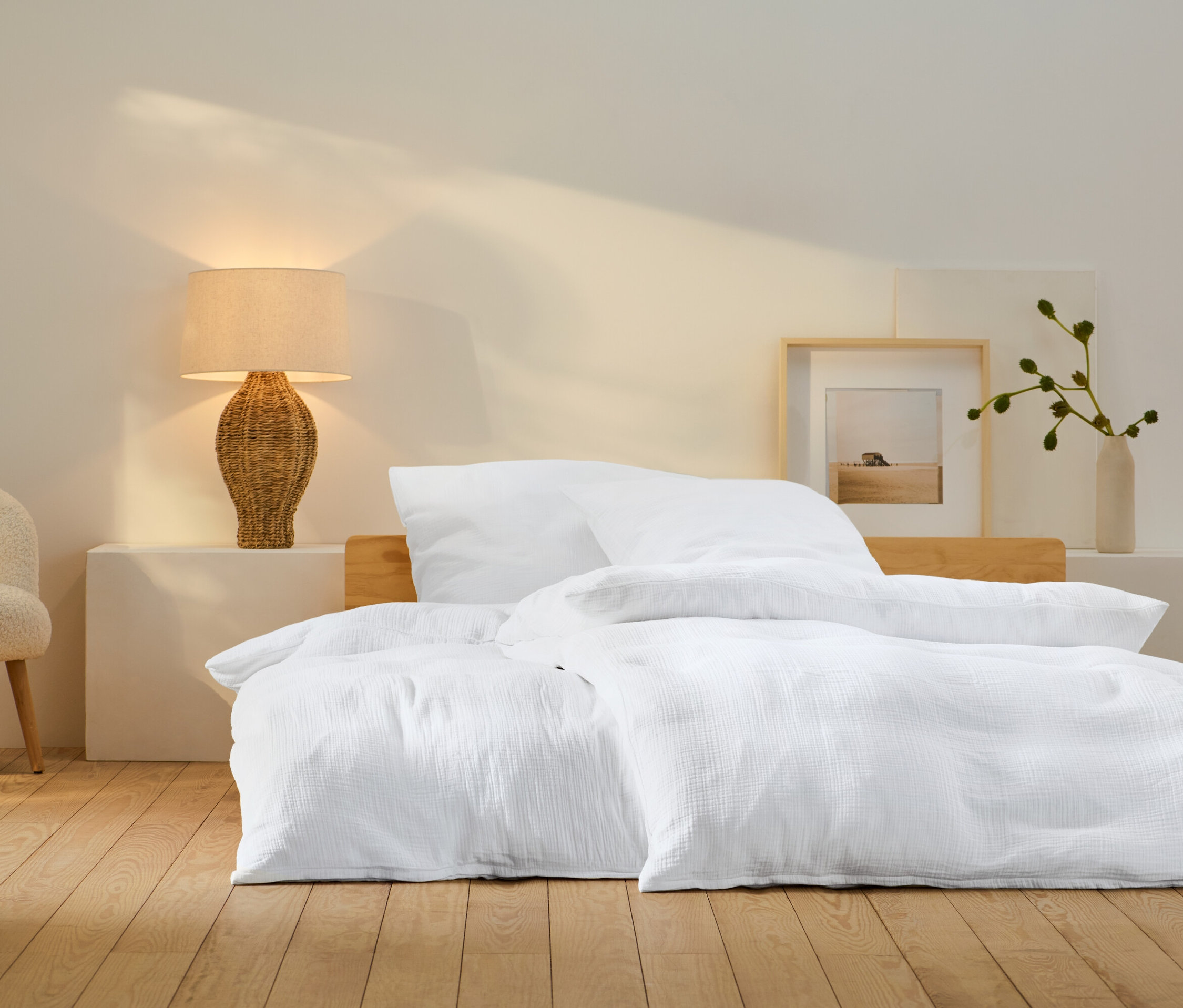 Chambre avec du linge de lit blanc sur le lit, une lampe en osier et un fauteuil beige.