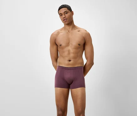 Un homme pose devant un fond clair, portant un caleçon boxer bordeaux.