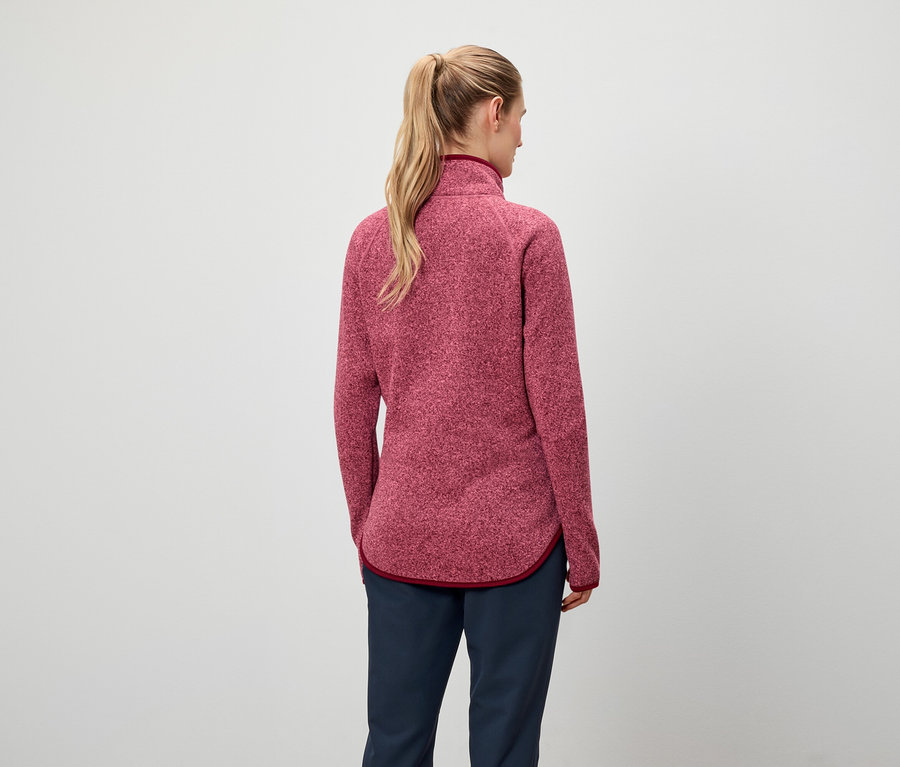 Vue de dos, une femme aux cheveux blonds attachés en queue de cheval porte un sweat-shirt rouge et un pantalon bleu marine.