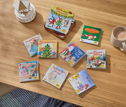 Sur une table en bois sont posés des livres pour enfants, une tasse avec une boisson et une petite décoration.