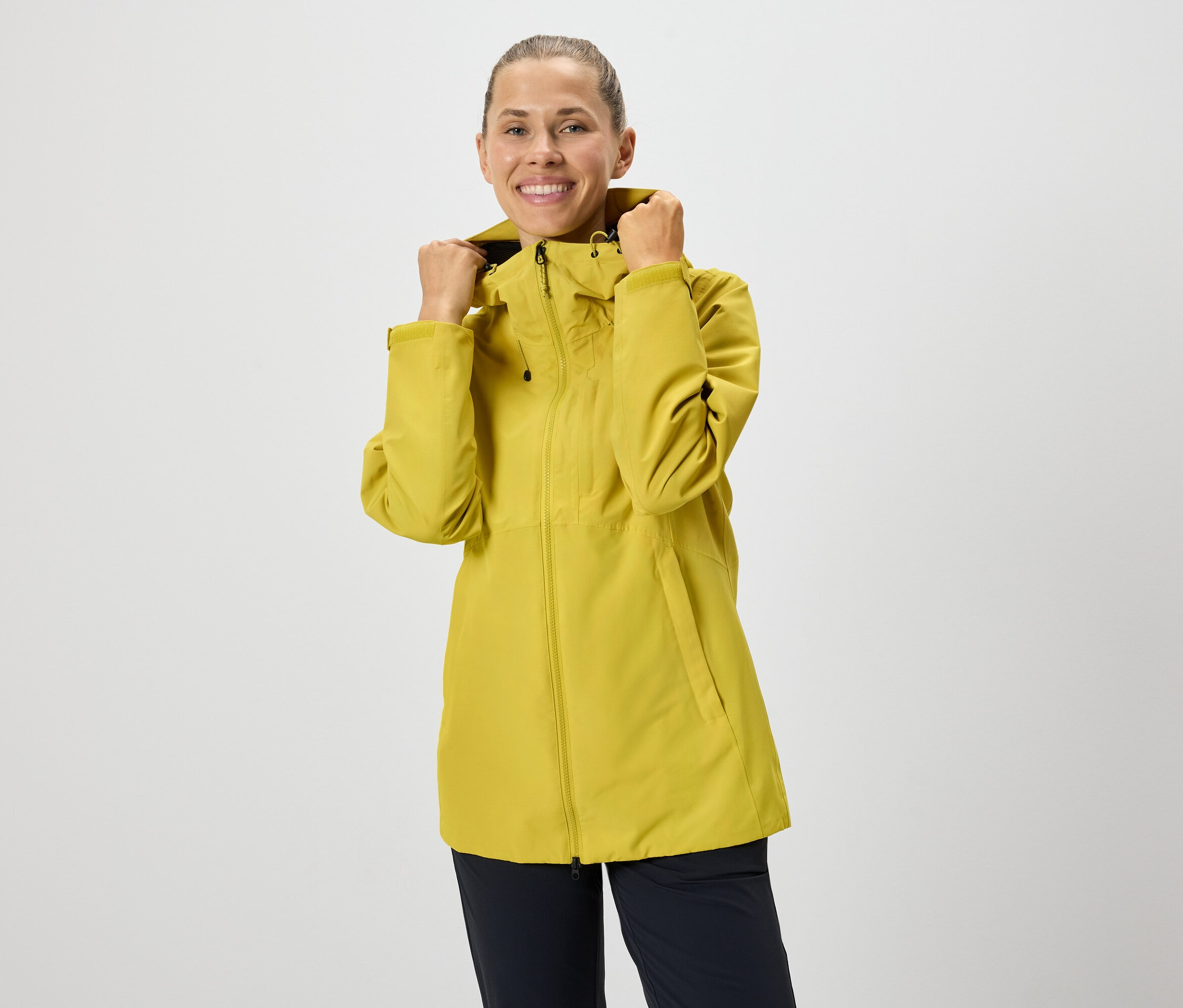 Femme ajustant la capuche d'une veste jaune à fermeture éclair.