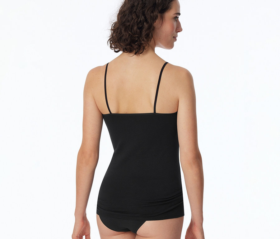Femme de dos, portant un top SCHIESSER noir et des sous-vêtements noirs. Elle regarde vers la droite.