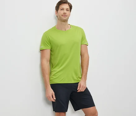 Un homme appuyé contre un mur porte un t-shirt technique lime et un short noir.