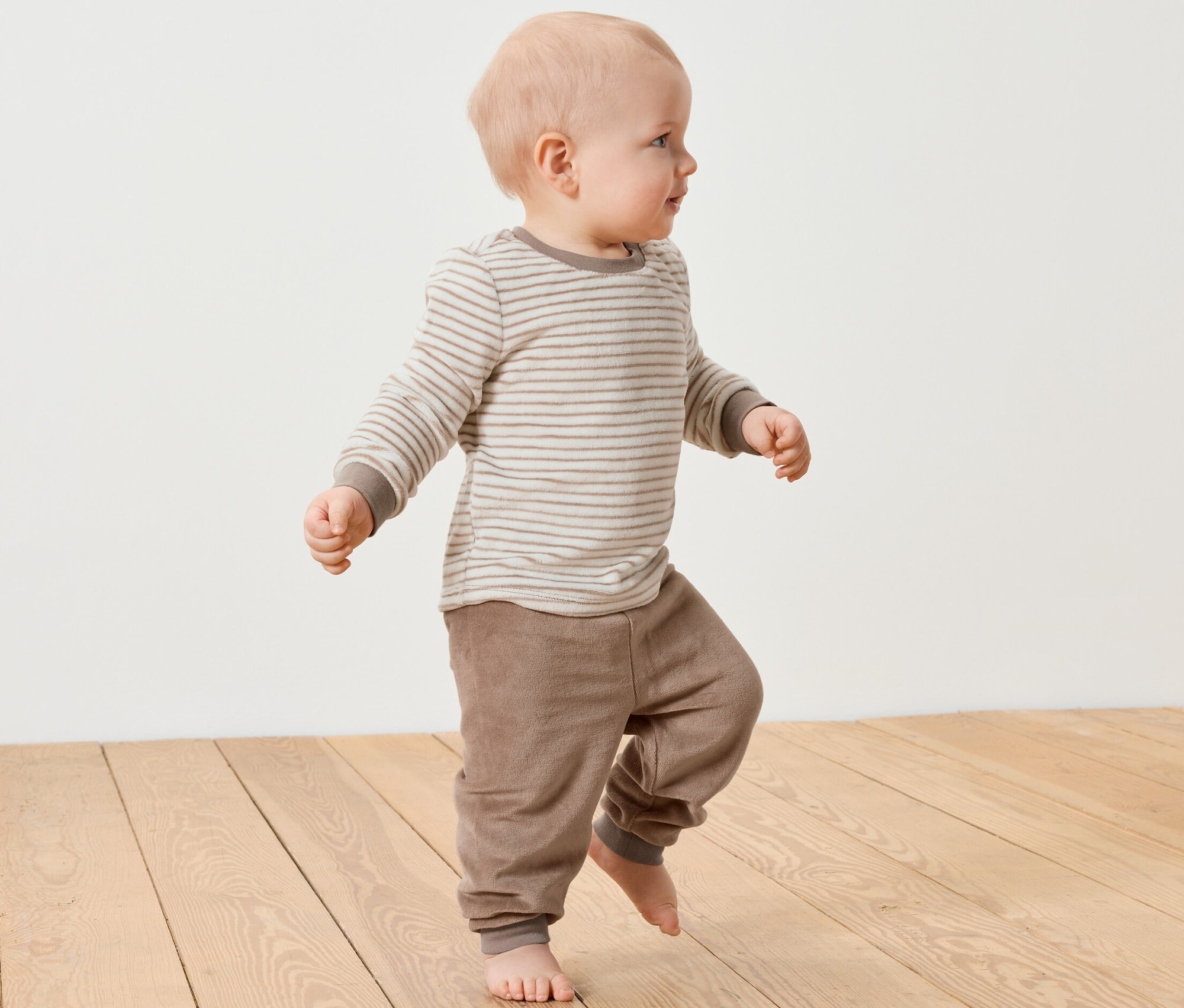 Un bébé marche sur un plancher en bois et porte un ensemble en nicki pour bébé.