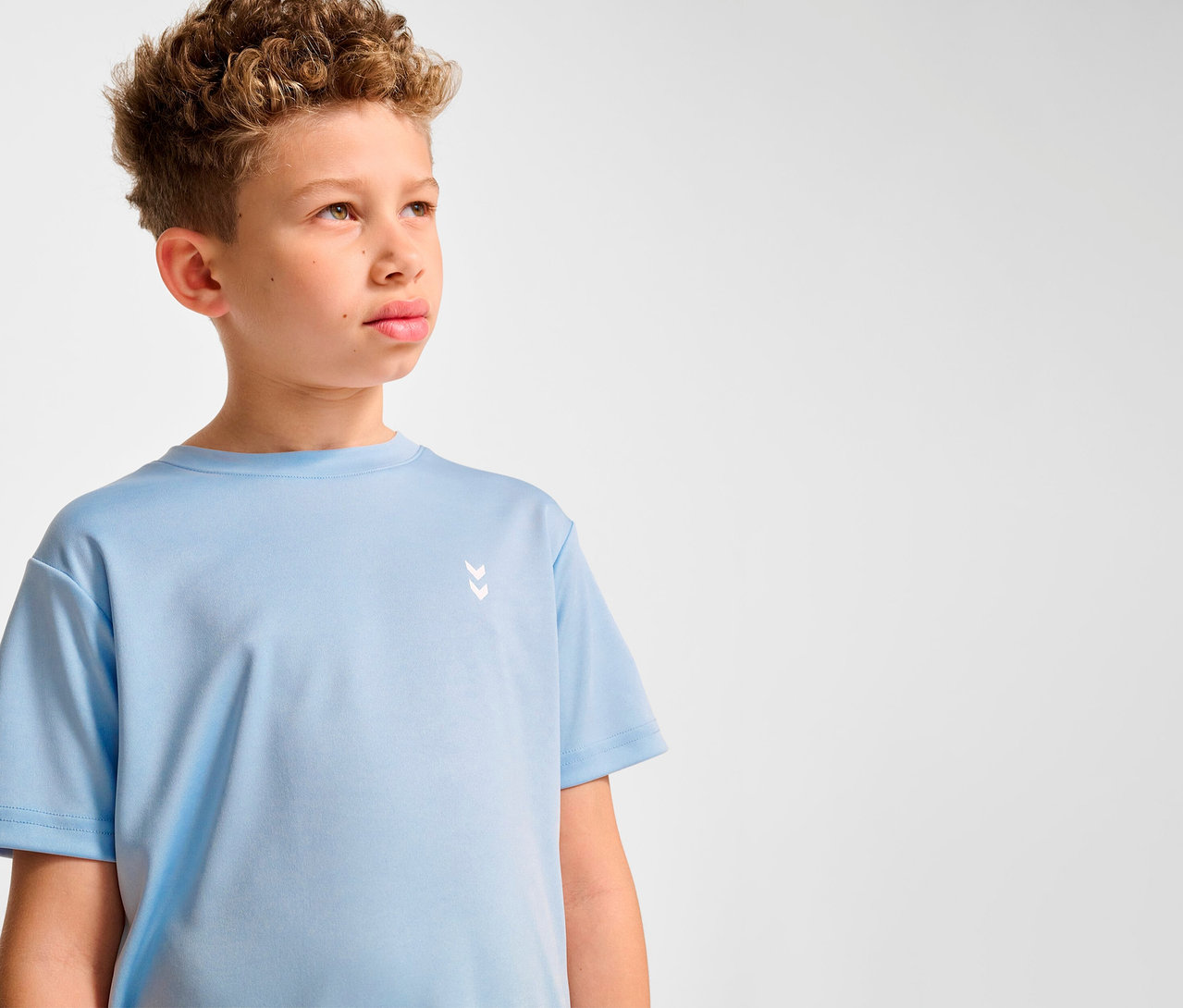 Garçon aux cheveux bouclés portant un t-shirt d'entraînement HUMMEL HMLJR pulse bleu clair.