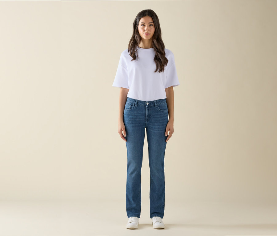 Une femme se tient debout et porte un t-shirt blanc, un jean bleu et des baskets blanches.