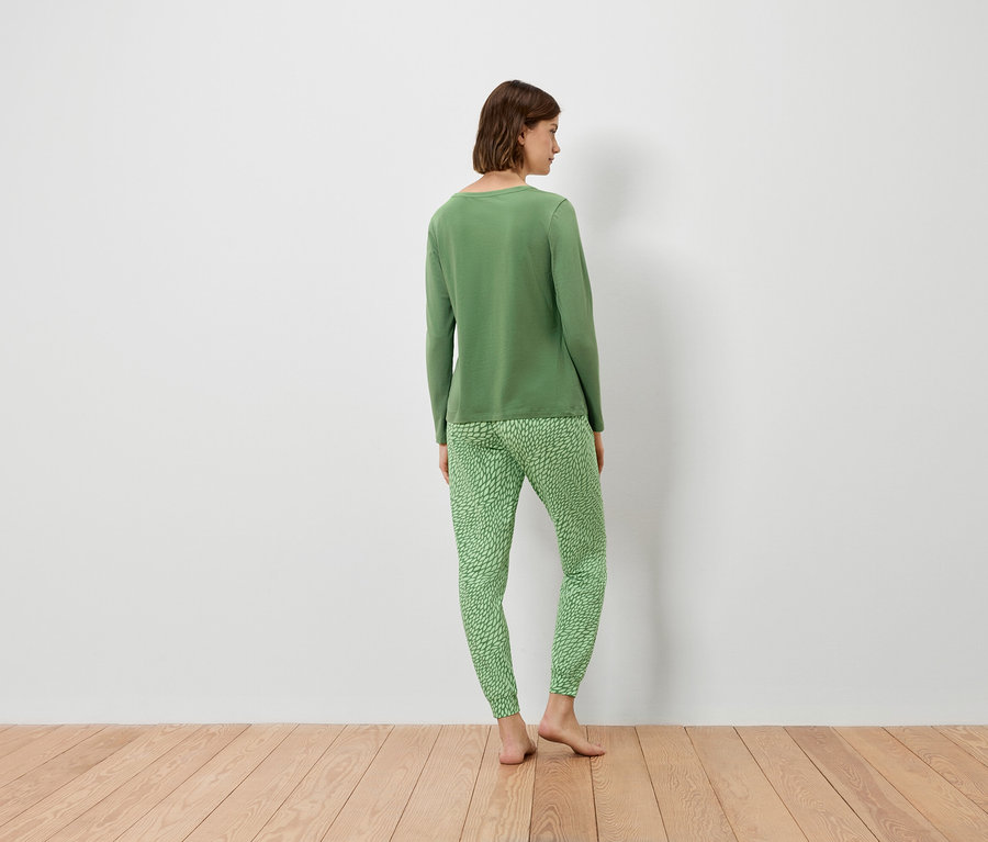 Une femme, vue de dos, porte un pull vert et un pantalon vert.