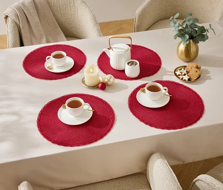 Quatre tasses sur des sets de table rouges sur une table avec une nappe blanche.