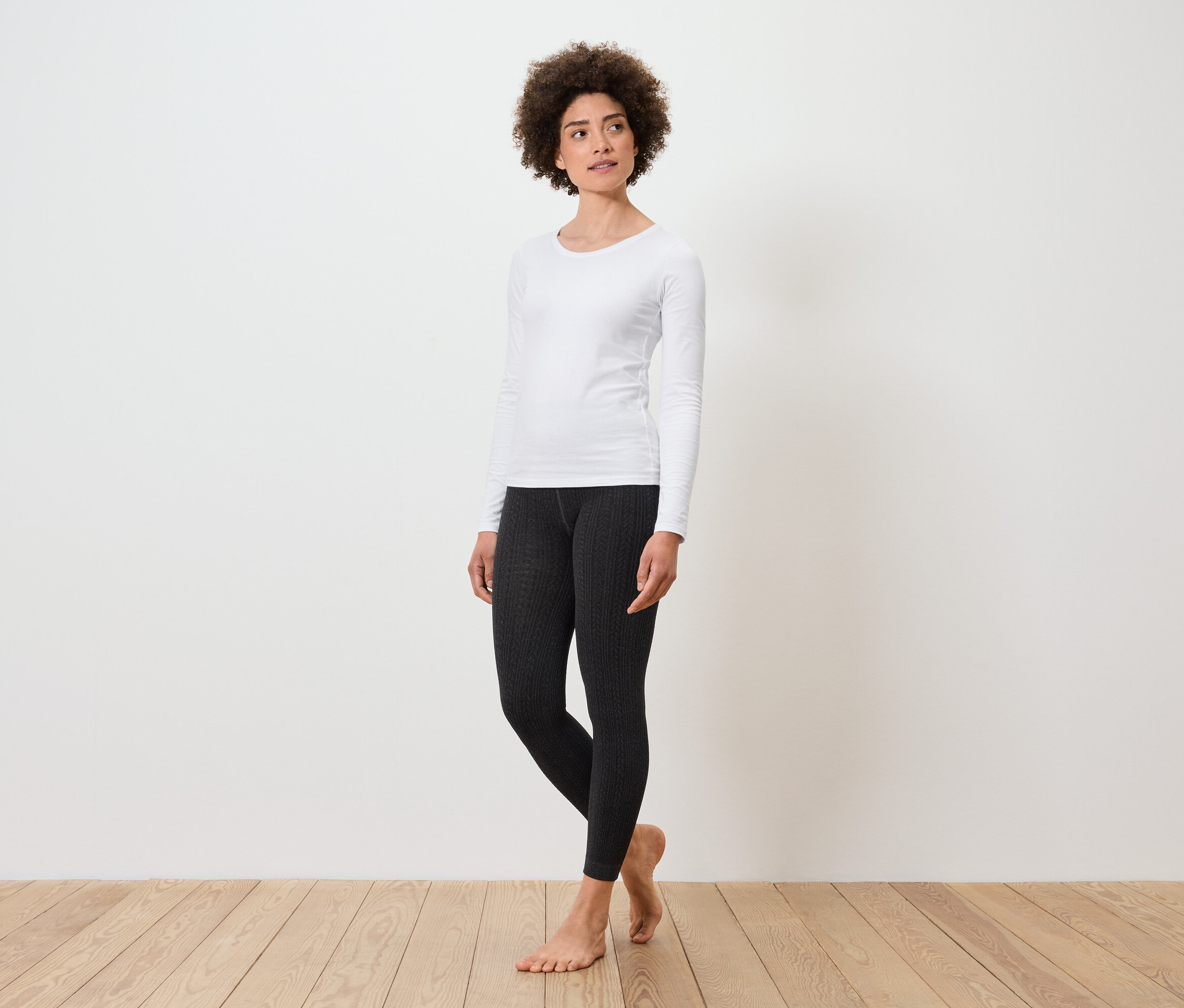 Une femme debout porte un t-shirt blanc à manches longues et un legging noir.
