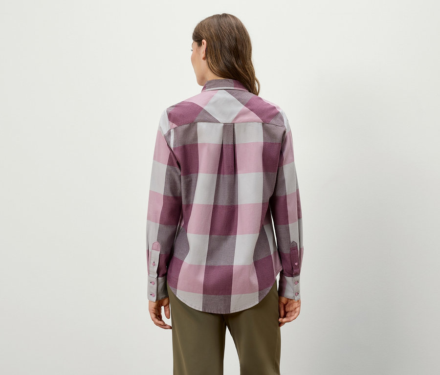 Vue de dos, une femme porte une chemise à carreaux à manches longues et un pantalon vert.