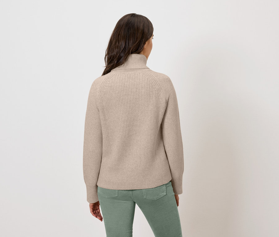 Vue arrière d'une femme portant un pull à col roulé beige et un pantalon vert.