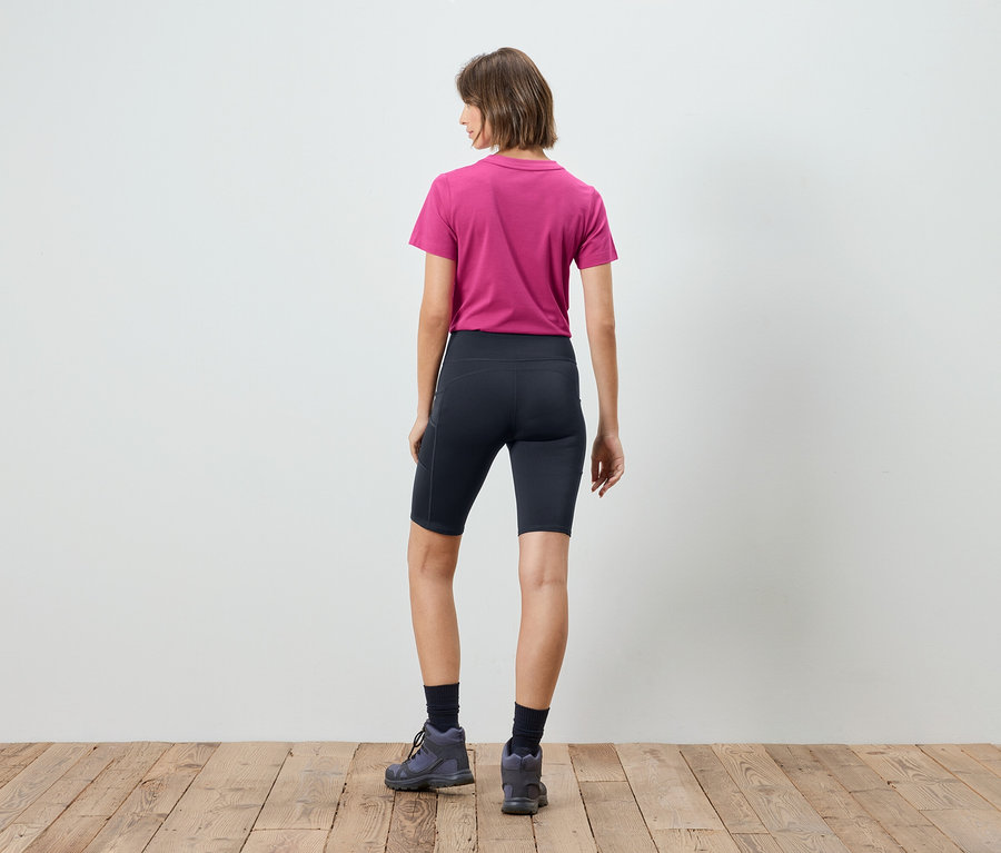 Vue de dos d'une femme aux cheveux courts bruns portant un t-shirt rose à manches courtes, un legging court bleu marine, des chaussettes bleu marine et des chaussures de randonnée grises.