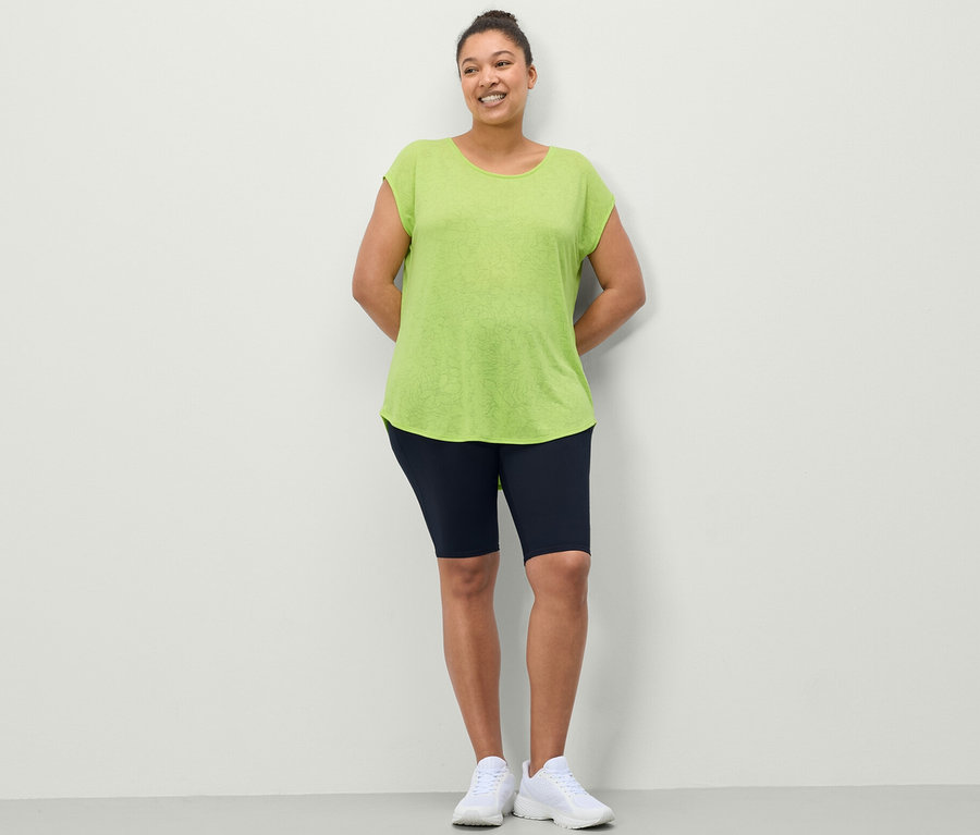 Femme posant en cycliste de sport bleu foncé et t-shirt de sport vert citron.