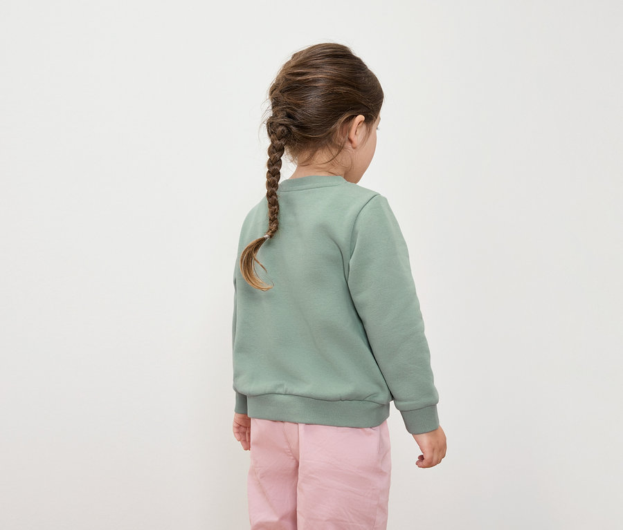 Vue arrière d'une fillette avec une tresse, vêtue d'un sweat-shirt vert et d'un pantalon rose.