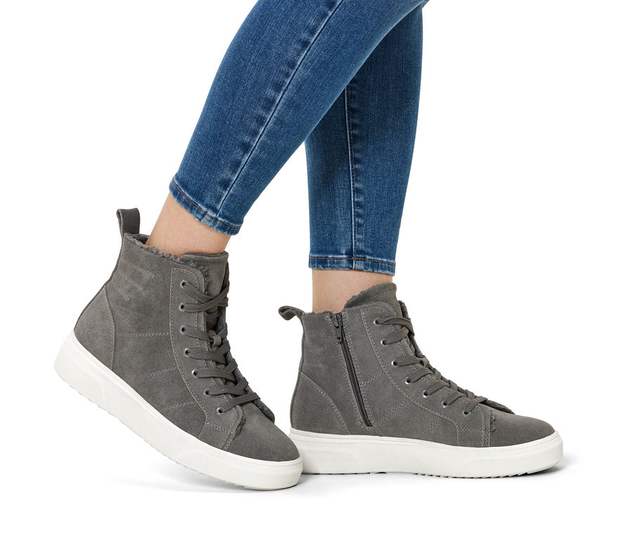 Jambes en jean bleu et bottes en daim grises à semelles blanches.