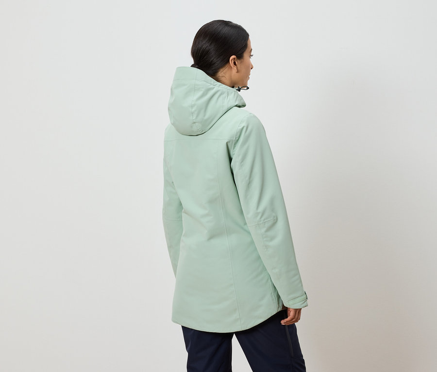 Vue arrière d'une femme portant une veste à capuche vert menthe et un pantalon bleu marine.