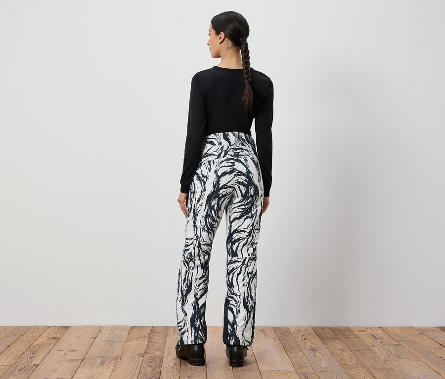 Femme vue de dos portant un haut noir à manches longues et un pantalon à motifs noir et blanc.