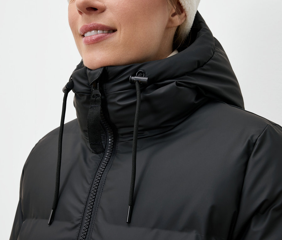 Une femme porte une doudoune noire et un bonnet blanc.