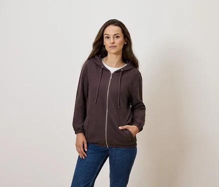Femme posant dans un sweat à capuche marron zippé et un jean bleu.