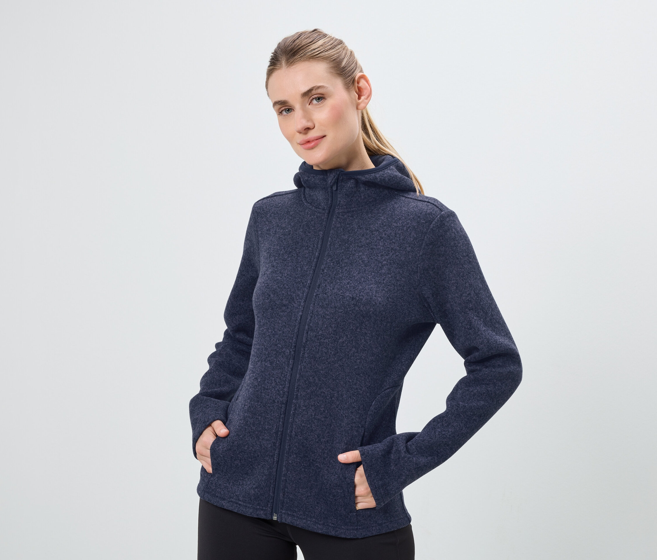 Une femme porte un sweat à capuche bleu marine zippé et un pantalon noir.