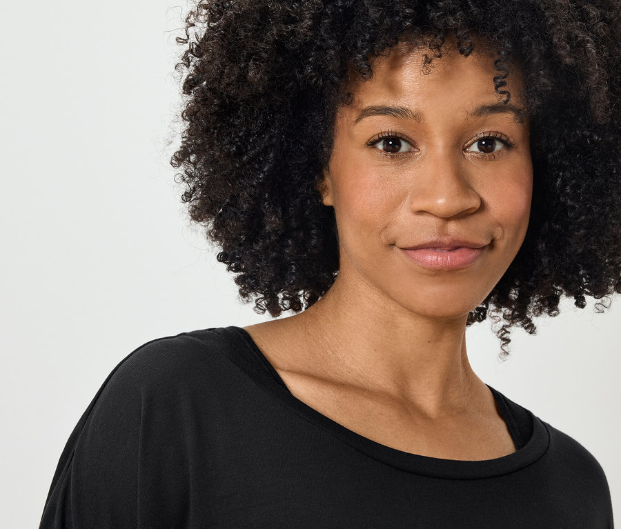 Portrait d'une femme souriante aux cheveux bouclés portant un t-shirt noir.