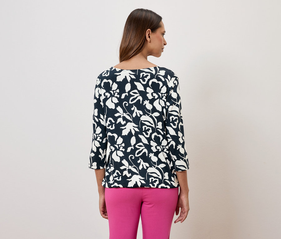 Femme vue de dos, portant un chemisier bleu marine à fleurs avec des manches trois-quarts et un pantalon rose.