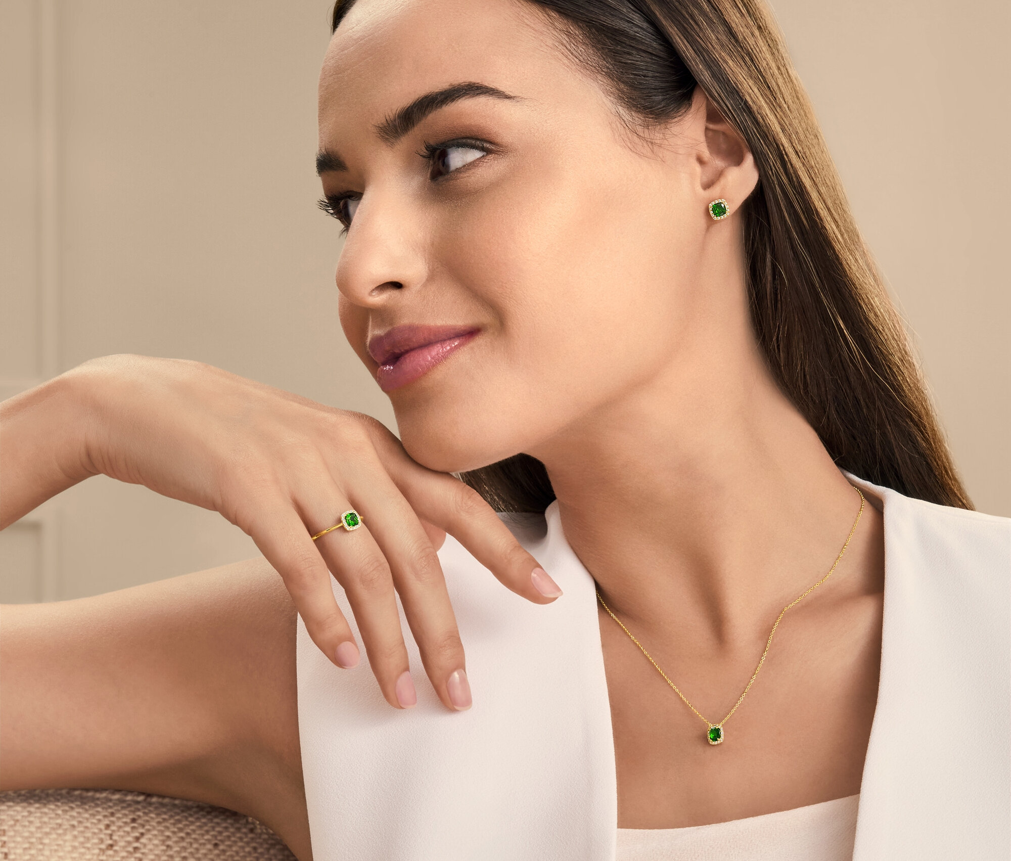 Une femme portant un collier, des boucles d'oreilles et une bague avec des pierres vertes.