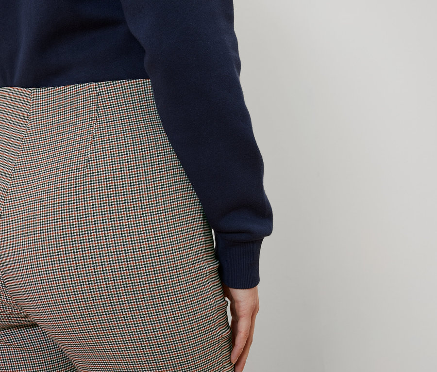 De dos, une femme porte un pull bleu marine et un pantalon à carreaux.