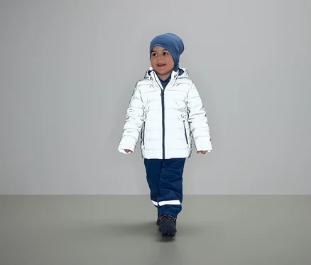 Un garçon marche dans une doudoune blanche, un pantalon bleu et un bonnet.