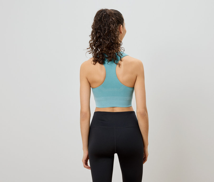 Vue arrière d'une femme aux cheveux bouclés portant un soutien-gorge de sport turquoise à dos nageur et un legging noir.