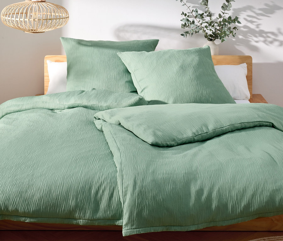 Lit avec des draps et des oreillers vert clair sur un cadre de lit en bois.