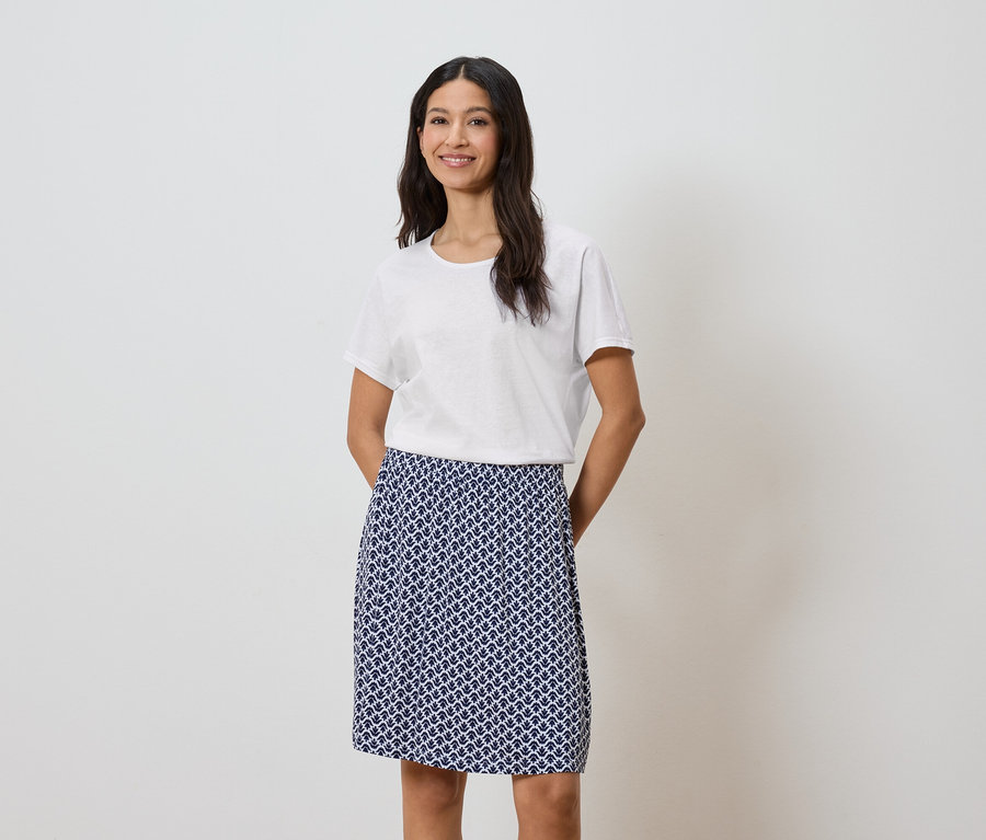 Femme portant un t-shirt blanc et une jupe bleue à motifs.