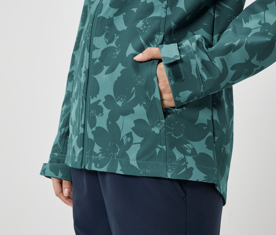 Personne avec la main dans la poche d'une veste à motifs vert et bleu, portant un pantalon bleu.