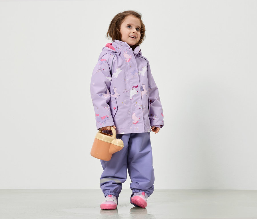 Une fillette vêtue d'un imperméable violet à motifs de licornes tient un arrosoir.